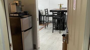 Een compacte keuken met een koelkast, koffiezetapparaat en een eethoek met stoelen en een tafel.