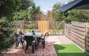 Une terrasse avec une table et des chaises, entourée d’une clôture en bois et de verdure.