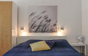 Une chambre à coucher avec un lit, une lampe fixée au mur et une table de chevet équipée d’un ventilateur.