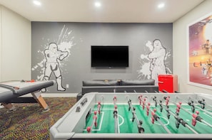 Une pièce équipée d’un baby-foot, d’une table de massage, d’un téléviseur et agrémentée d’œuvres d’art murales.