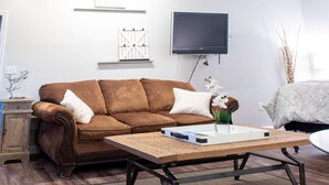 Un salon avec un canapé marron, une table basse, un téléviseur fixé au mur et un petit meuble.