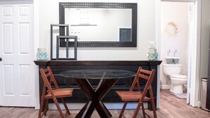 Un coin repas avec une table ronde en verre et des chaises en bois, une cheminée noire et une porte blanche.