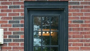 Une porte noire avec un panneau de verre, encastrée dans un mur de briques.