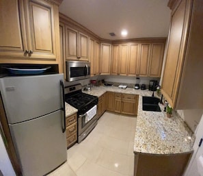 Una cocina con gabinetes de madera, un refrigerador de acero inoxidable, un microondas, una estufa y una encimera de granito.