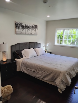 Un dormitorio con cama, mesitas de noche, una obra de arte en la pared, una ventana con vistas y una lámpara en el techo.
