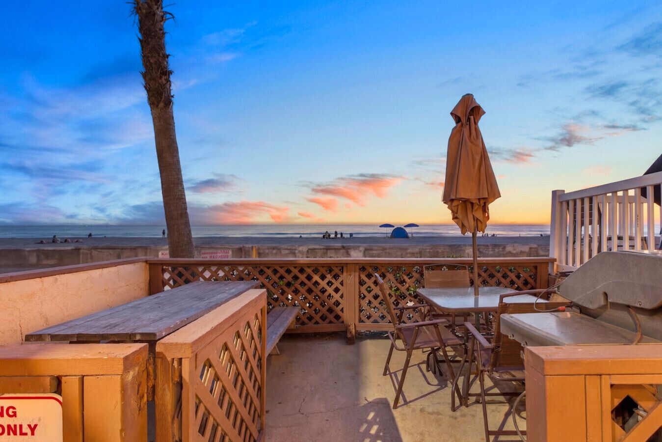 Une terrasse au bord de la plage, avec des meubles en bois, un palmier et une vue sur l’océan.