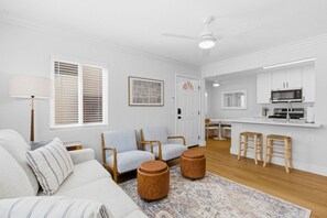 Una sala de estar con sofá, sillones, una mesa de centro y una zona de cocina con microondas y taburetes de bar.