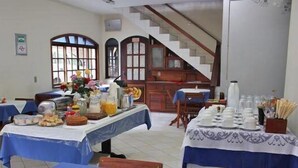 Une salle à manger avec des tables dressées pour le repas, un escalier et, au fond, une cuisine.