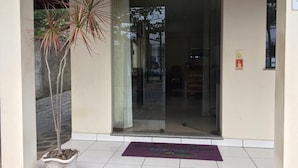 Une entrée d’immeuble avec une porte en verre, une plante en pot et un paillasson.