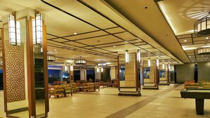 Un grand espace intérieur aménagé avec différents types de sièges, notamment des bancs et des chaises, et une table de billard au centre.