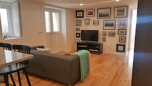 A living room with a sofa, a dining table, chairs, a TV, and a wall decorated with framed pictures. - Carmo Apartment in the center of Espinho (Espinho)