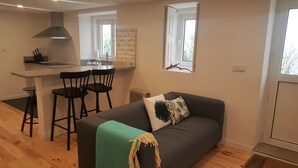 A compact living space with a kitchenette, a dining area with chairs, a sofa with a throw blanket, and a window with a view of trees. - Carmo Apartment in the center of Espinho (Espinho)
