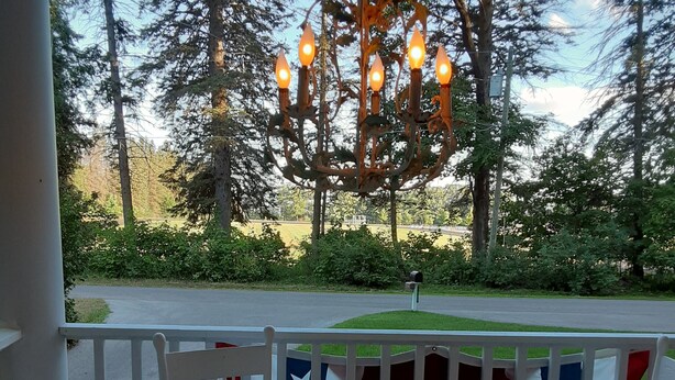 A table set for dining on a porch with a view of trees and a flag. - 3,200SF Home/ 3.5 Bathrooms-3 Showers/Wrap Around Porch/Walk to Town/Beach (Harbor Springs)