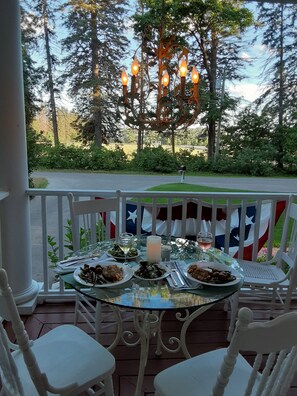 A table set for dining on a porch with a view of trees and a flag.