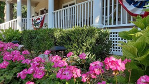 A porch with a white railing, a flag, and pink flowers. - 3,200SF Home/ 3.5 Bathrooms-3 Showers/Wrap Around Porch/Walk to Town/Beach (Harbor Springs)