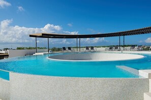 A large, circular infinity pool with a covered area and lounge chairs.