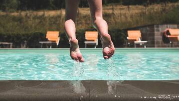 Piedi di una persona a mezz'aria mentre saltano in una piscina, con sedie a sdraio sullo sfondo.