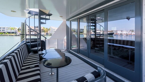 Une terrasse extérieure moderne, dotée d’un canapé rayé noir et blanc, d’une petite table ronde et d’une balustrade en verre donnant sur une marina.