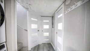 Un couloir avec des portes blanches, un escalier et un porte-manteau.