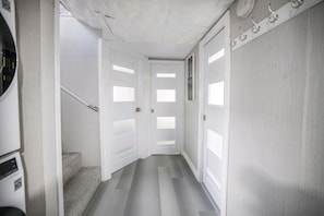 Un couloir avec des portes blanches, un escalier et un porte-manteau.