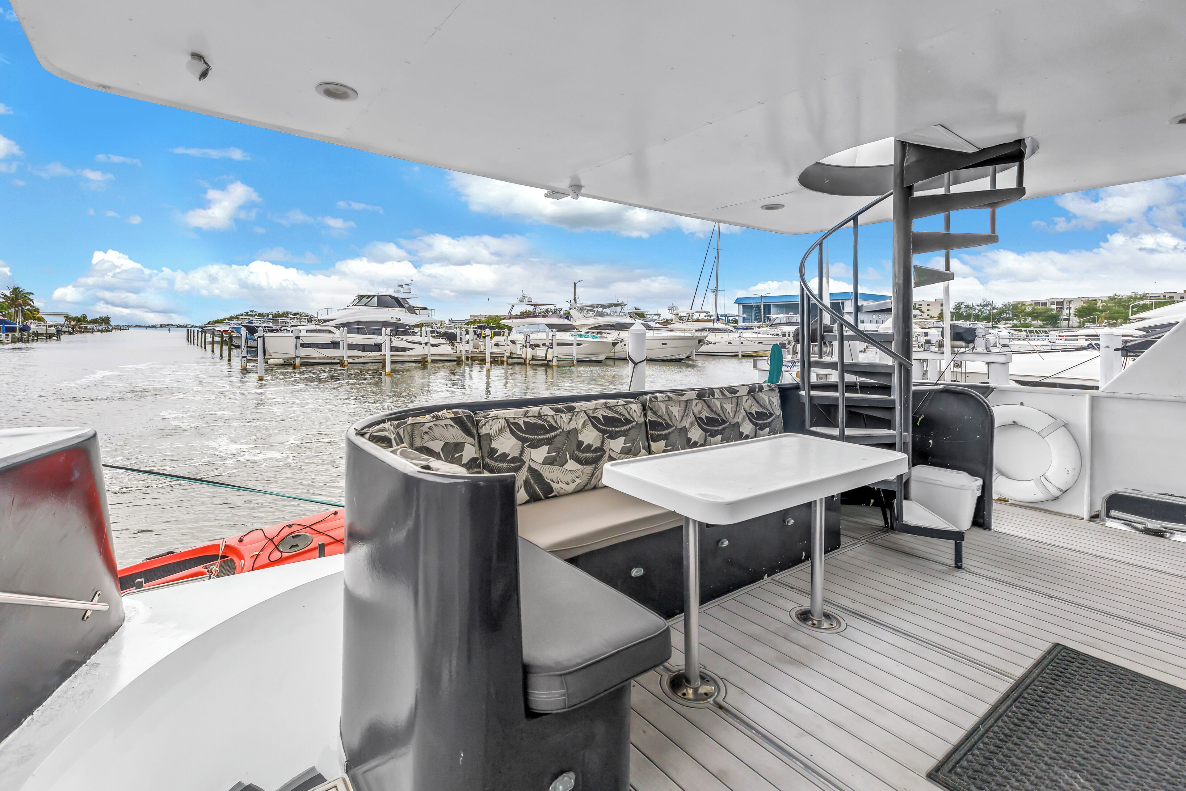 Ein Bootsdeck mit Sitzgelegenheit, einem Tisch und Blick auf den Yachthafen mit weiteren Booten.