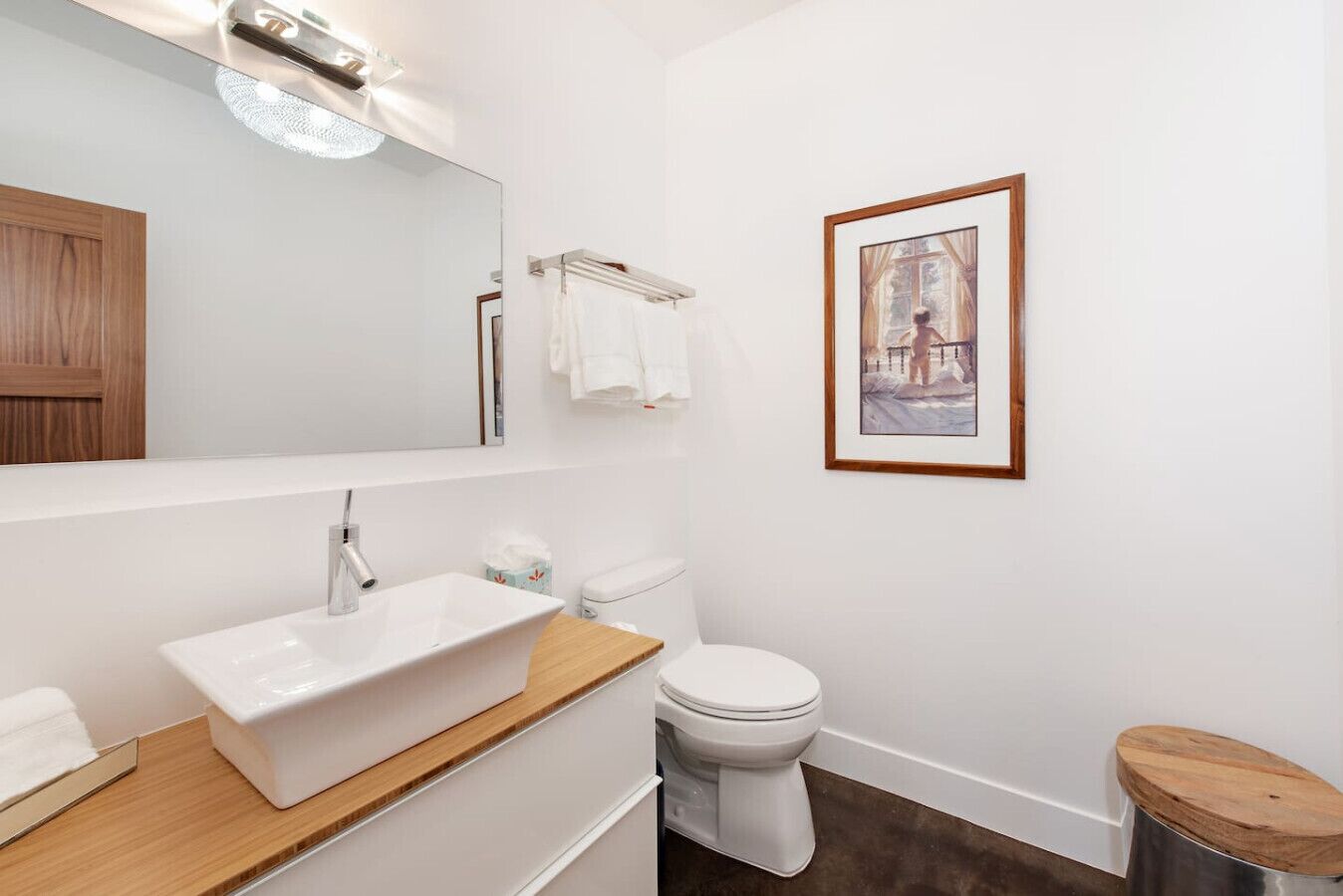 Une salle de bain moderne avec un grand miroir, un lavabo blanc, des toilettes et un tableau encadré au mur.
