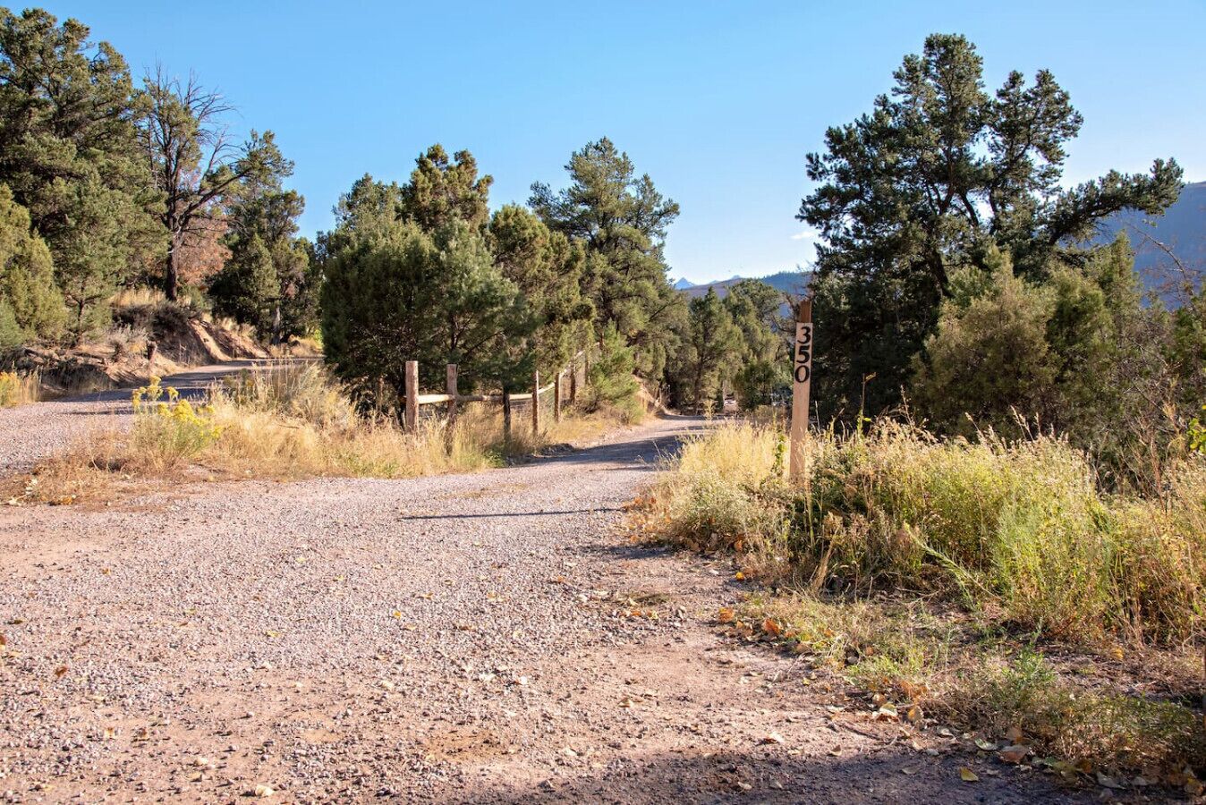 Un camino de grava que serpentea por un área boscosa con una verja de madera y un cartel.