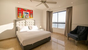 Una habitación de hotel con una cama grande, un ventilador de techo, una ventana con cortinas y una silla.