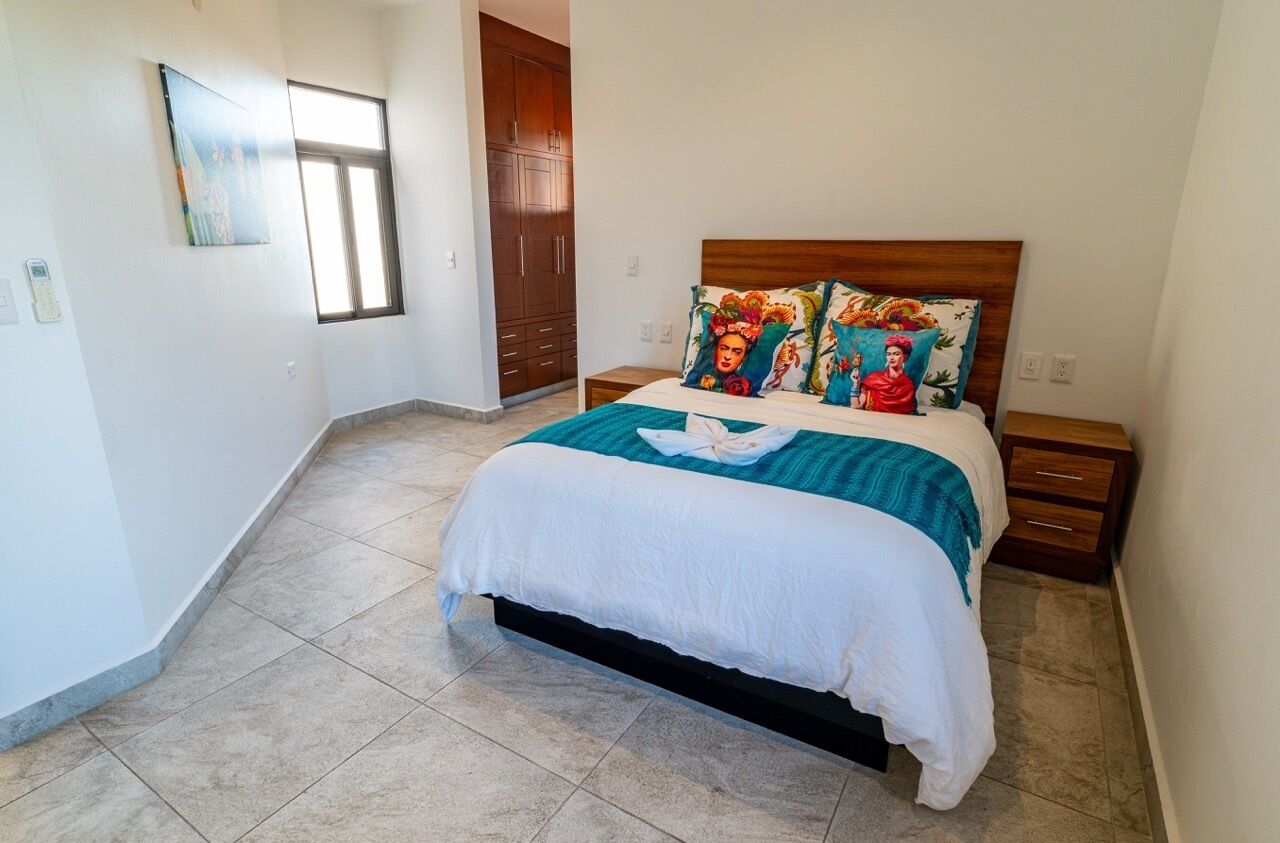 A bedroom with a bed, a nightstand, a wooden wardrobe, and a window.