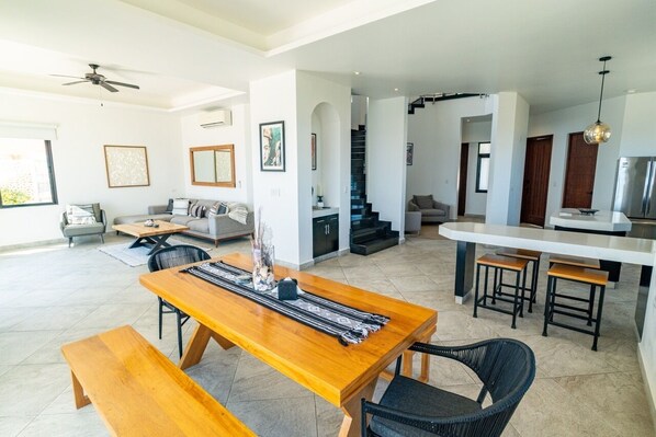 A spacious living area with a wooden dining table, sofas, and a kitchen area with bar stools.