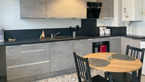 A modern kitchen with grey cabinets, a black countertop, a wooden dining table, and a hanging light fixture.