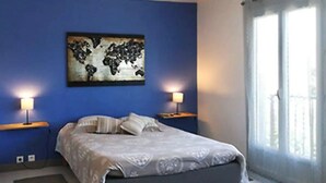 A bedroom with a bed, two bedside lamps, a wall-mounted artwork, and a window with curtains.
