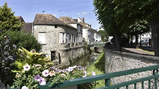 A stone building with a canal in front, surrounded by greenery and a green railing.