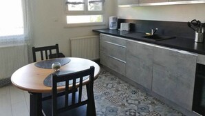 A compact kitchen with a round table, chairs, a coffee maker, and a clock on the wall.