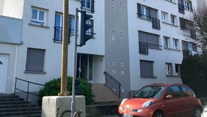 A multi-story residential building with balconies, a staircase, and a red car parked in front.