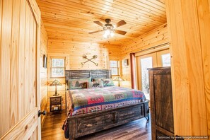 A cozy wooden cabin bedroom with a bed, a ceiling fan, and a window.