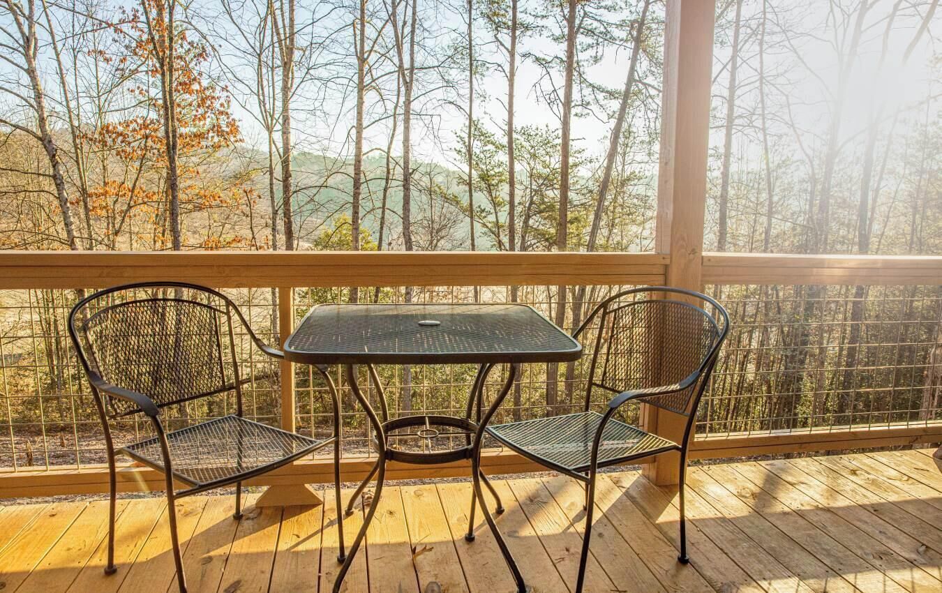 Une terrasse en bois avec une table en métal et deux chaises, donnant sur une zone boisée.