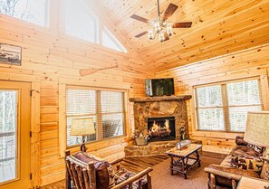 L’intérieur d’une cabane en rondins, avec une cheminée en pierre, des meubles en bois et de grandes fenêtres.