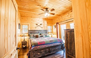 Une chambre confortable, aménagée dans un chalet en bois, avec un lit, un ventilateur de plafond et une fenêtre.