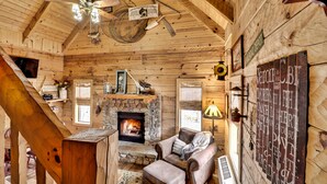 A cozy log cabin interior with a stone fireplace, a leather sofa, and a ceiling fan.