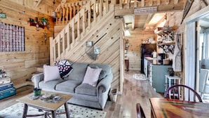A wooden cabin interior with a staircase, a sofa, a table, and a kitchen area.