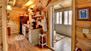 A wooden cabin interior with a kitchen, dining area, and a large window.