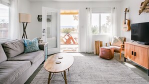 A modern living room with a sofa, coffee table, and a TV. There's a balcony with a view.