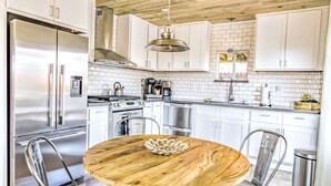 A modern kitchen with white cabinets, stainless steel appliances, a round wooden table, and metal chairs.