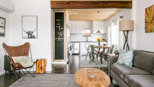 A modern living room with a sofa, a wooden coffee table, a leather chair, and a dining area with a table and chairs.