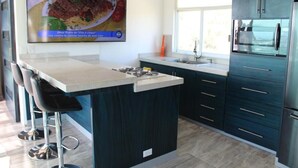 A modern kitchen with a central island, bar stools, a built-in oven, and a large window.