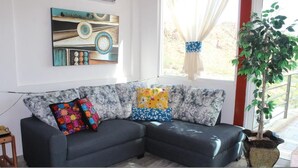 A modern living room with a dark grey sectional sofa, colorful patterned cushions, a wall art piece, and a potted plant.