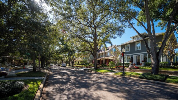 A residential street lined with houses, trees, and a clear sky.