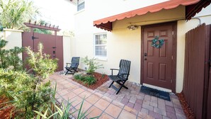 A patio with two chairs, a door with a wreath, and a small garden.