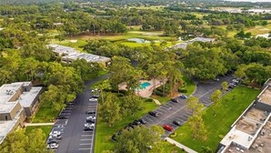 An aerial view of a golf course with a swimming pool, parking lots, and surrounding greenery.